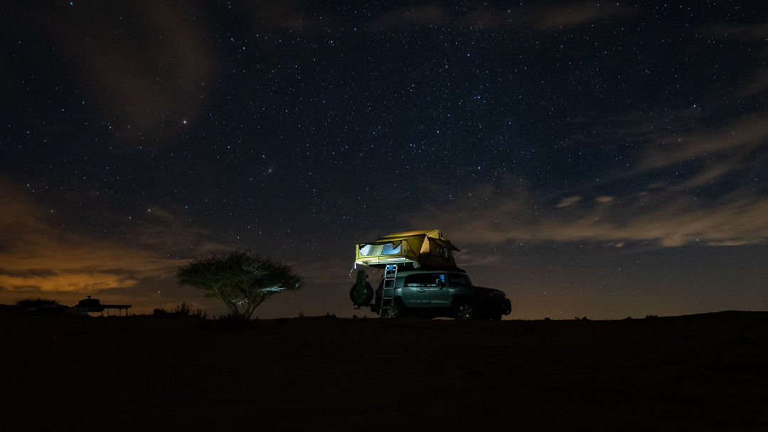 Night camping in the desert of Saudi Arabia. A tent sits atop a Toyota FJ, sillouetted by the star-filled sky. Photographed by 8d Photos based in Clermont, Florida, USA.